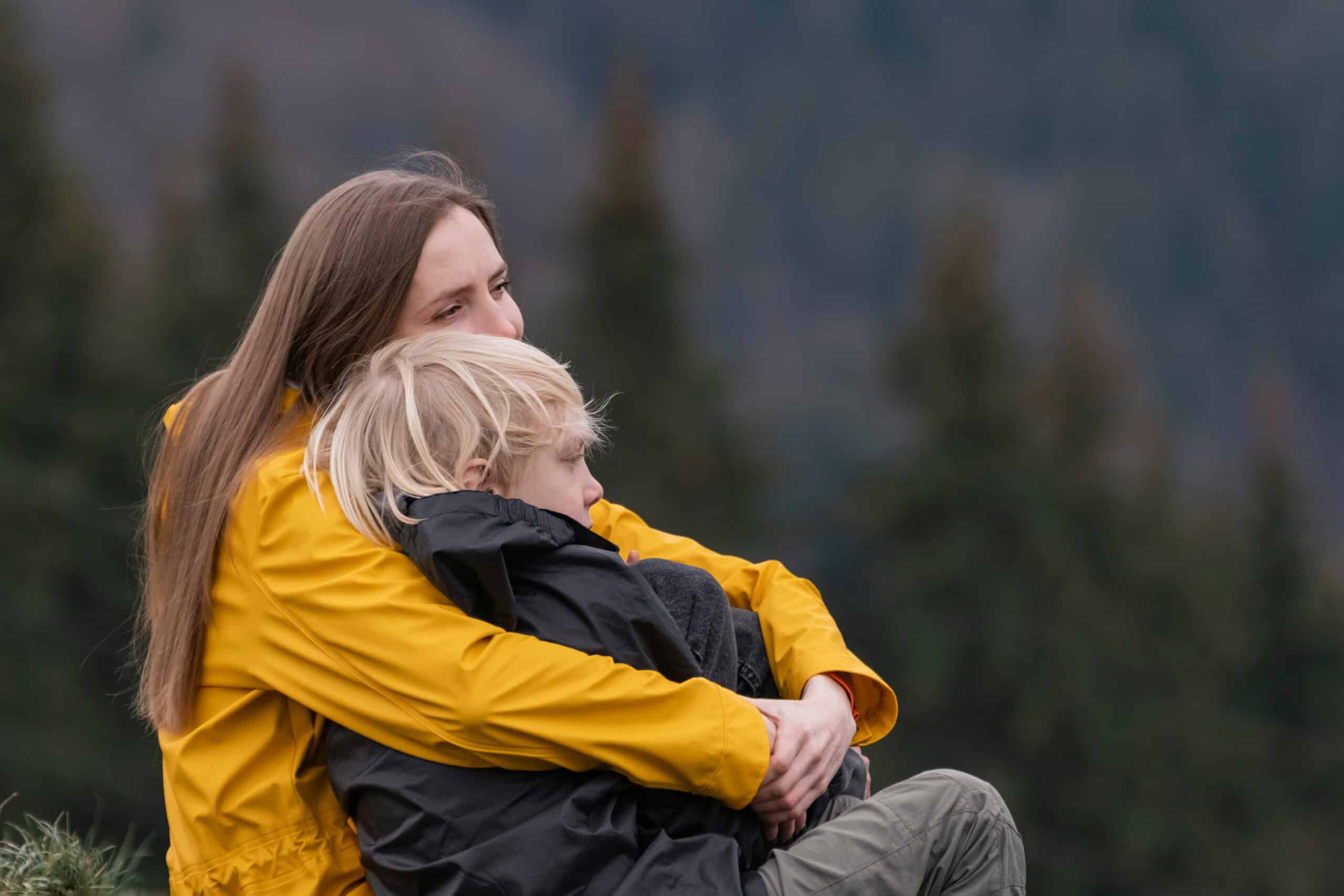 A mother sitting outdoors, holding and comforting her young son in a warm embrace