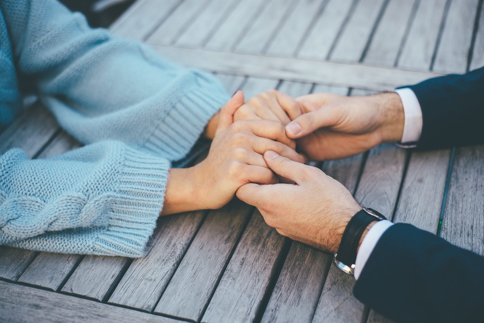 Two people holding hands across a wooden table.